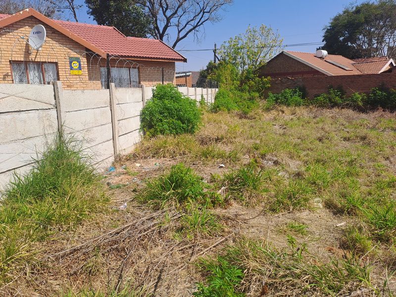 A vacant residential plot featuring a precast concrete boundary wall with security razor wire, adjacent to existing brick residential properties.