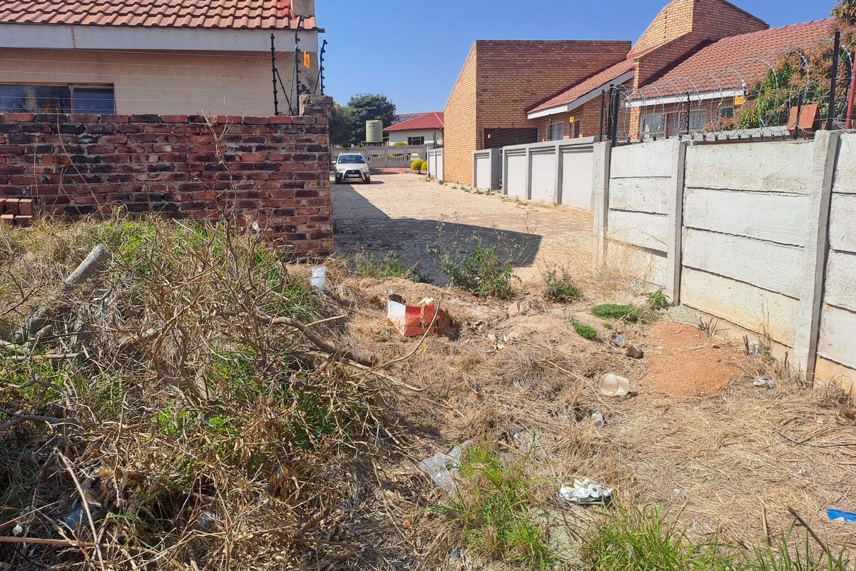 A view of the front access area featuring a paved driveway, brick and precast boundary walls, and electric fencing, currently requiring site clearing.