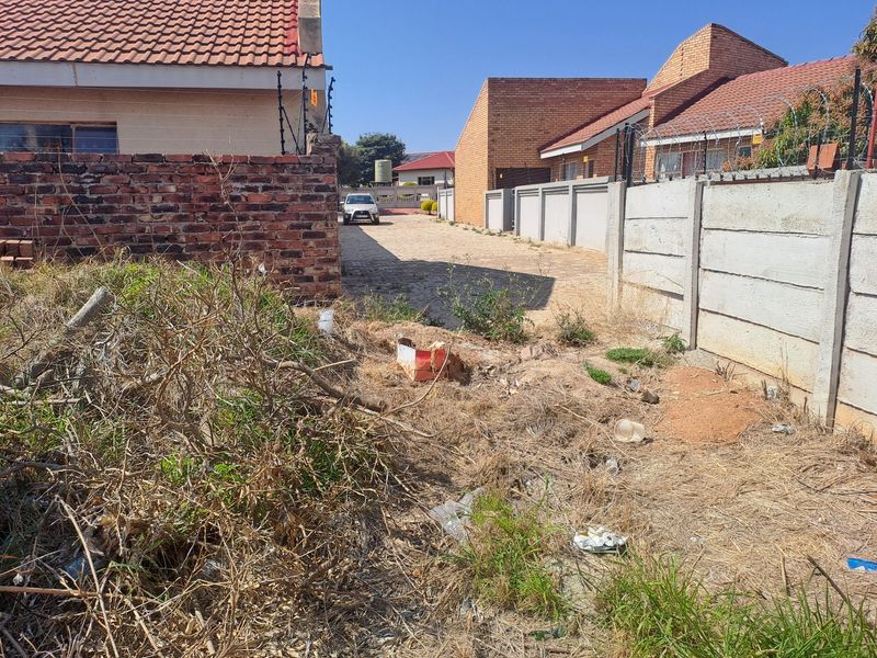 A view of the front access area featuring a paved driveway, brick and precast boundary walls, and electric fencing, currently requiring site clearing.