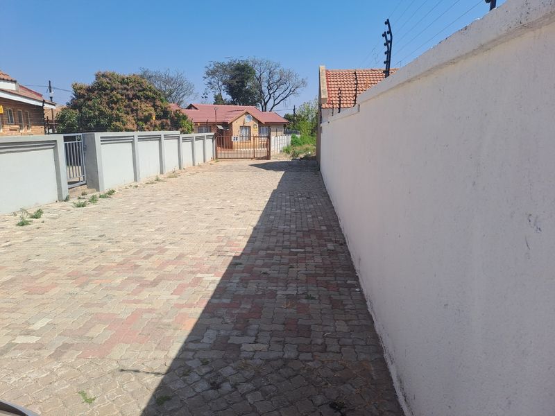 A paved driveway leading to a gated entrance, featuring perimeter walls with integrated electric fencing.