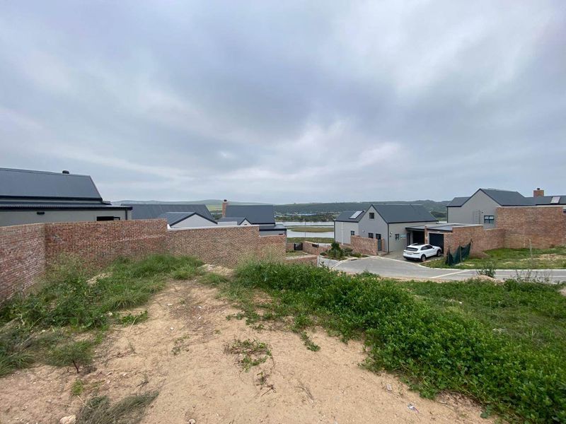 A view of a modern residential estate featuring brick boundary walls, paved driveways, and contemporary homes with pitched metal roofs under a cloudy sky.