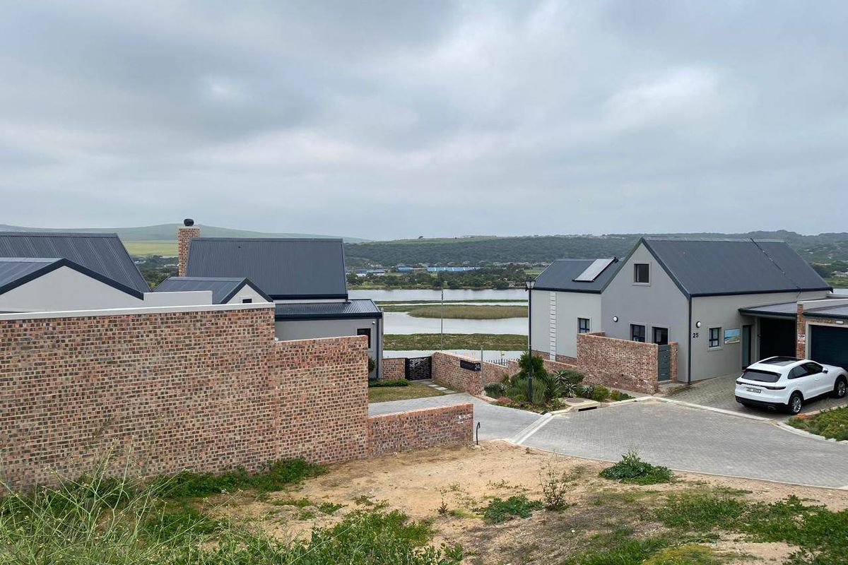 A view of the front exterior of modern residential houses featuring brick boundary walls, paved driveways, and metal roofing overlooking a scenic landscape.
