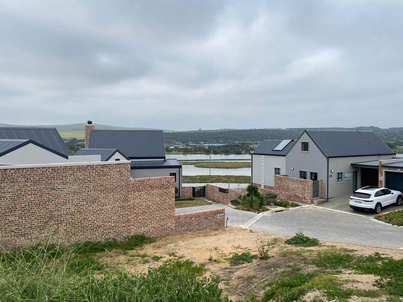 A view of the front exterior of modern residential houses featuring brick boundary walls, paved driveways, and metal roofing overlooking a scenic landscape.