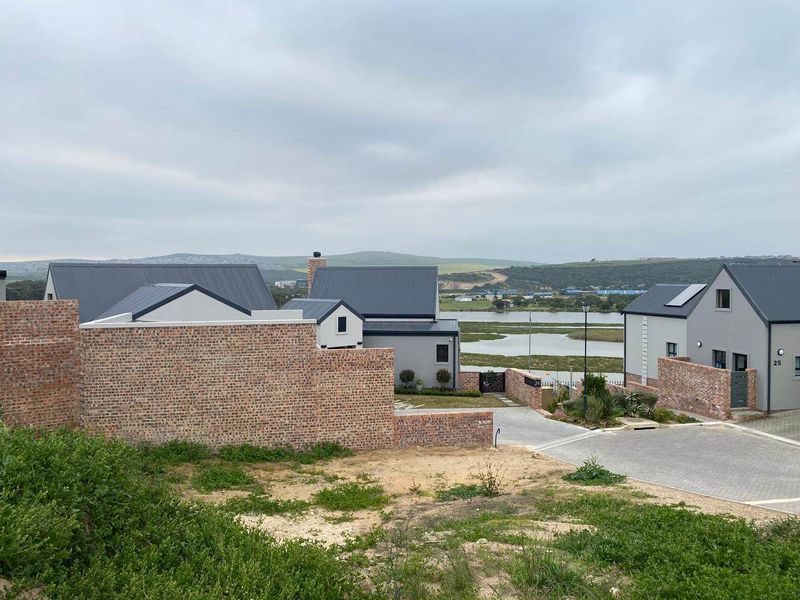 An elevated view of a modern residential estate featuring brick boundary walls, paved driveways, and contemporary homes with metal roofing overlooking a scenic wetland area.
