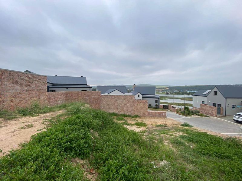 An elevated view of a residential estate featuring brick boundary walls, paved driveways, and modern homes with metal roofing under an overcast sky.