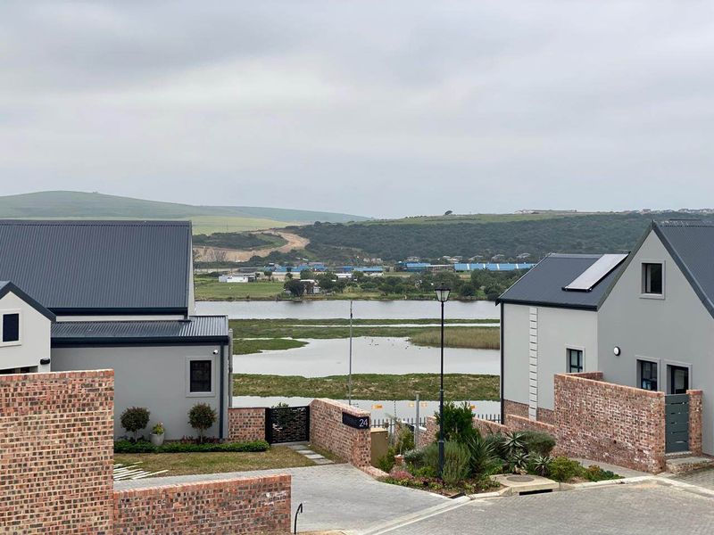 Elevated view overlooking a scenic wetland area, featuring modern residential architecture with metal roofing and brick boundary walls.