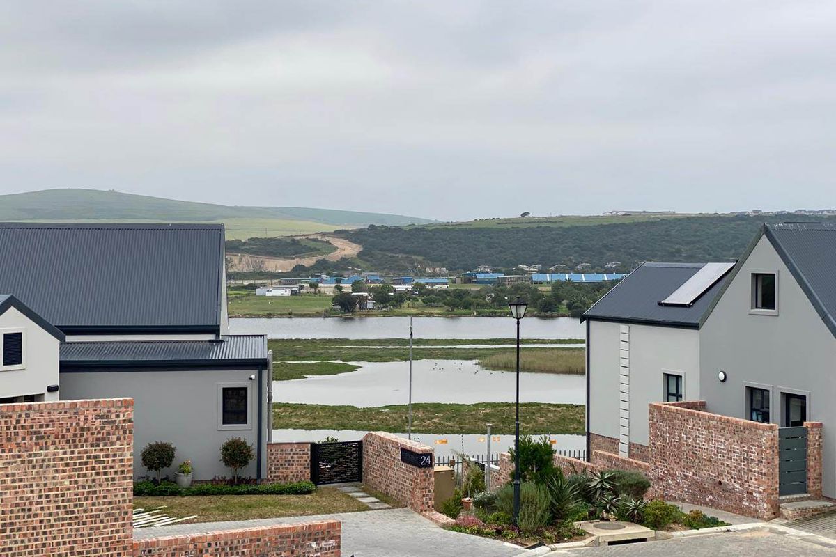 Elevated view overlooking a scenic wetland area, featuring modern residential architecture with metal roofing and brick boundary walls.
