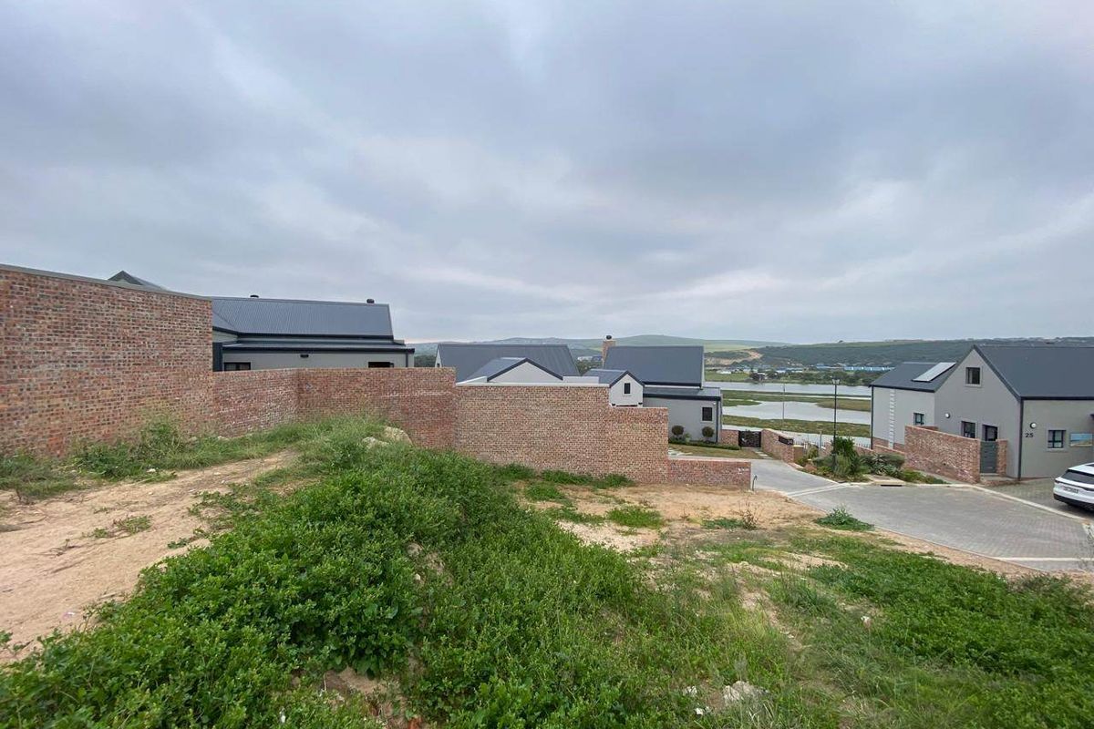 An elevated view of a residential estate featuring brick boundary walls, paved driveways, and modern homes with metal roofing under an overcast sky.