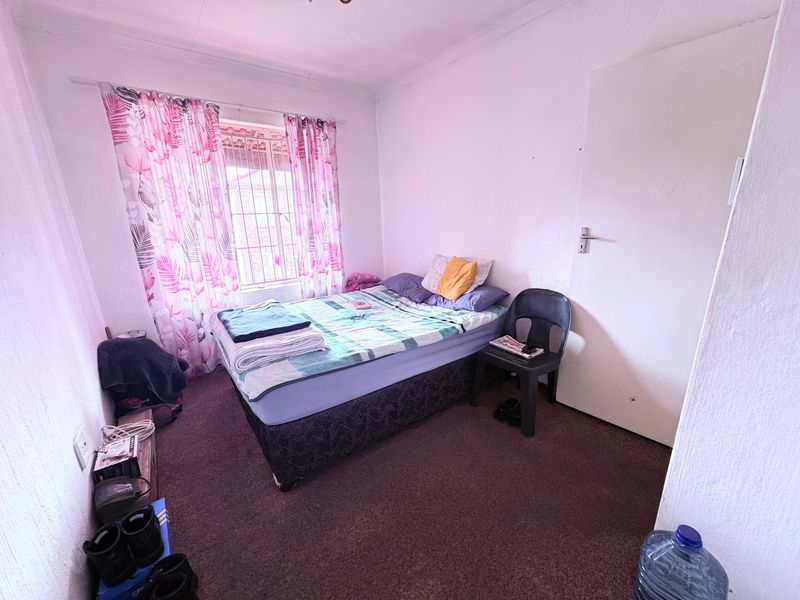 A functional bedroom featuring carpeted flooring, a window with security bars, and a standard internal door.