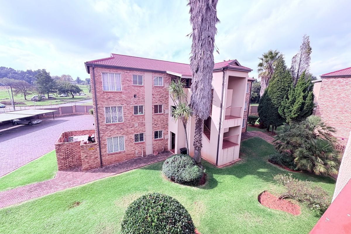 Aerial view of a multi-story brick apartment complex featuring landscaped gardens, paved parking areas, and covered carports.