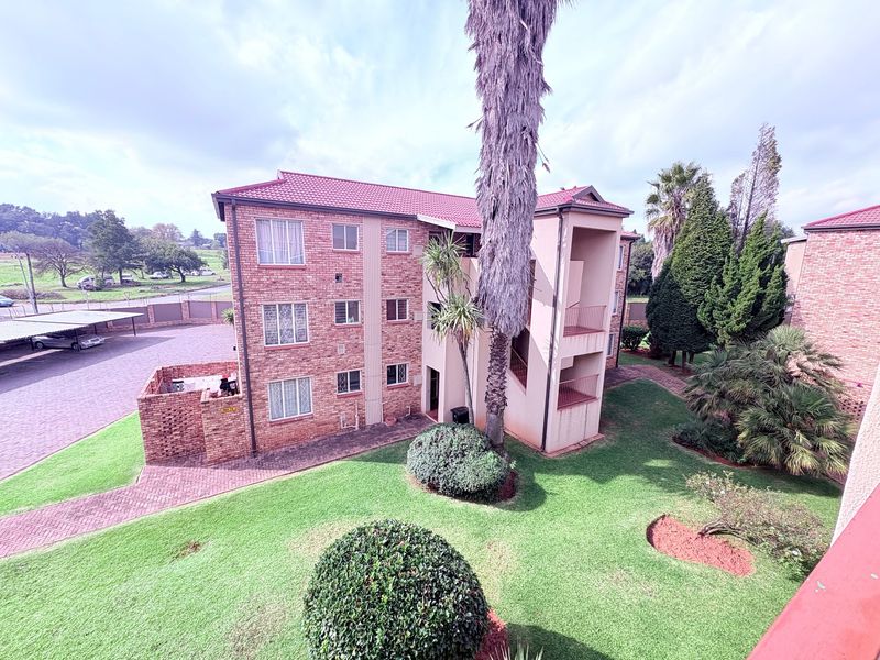 Aerial view of a multi-story brick apartment complex featuring landscaped gardens, paved parking areas, and covered carports.
