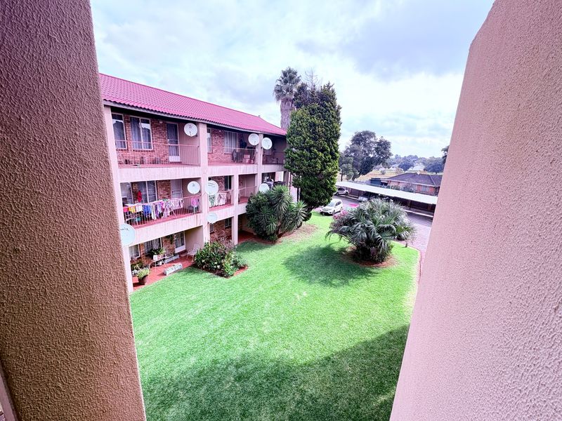 View of the apartment complex rear facade, featuring multi-level balconies overlooking a well-maintained communal garden and covered parking area.