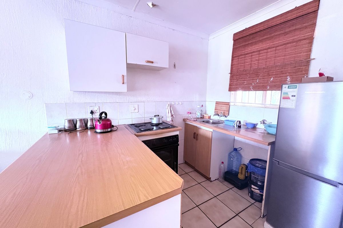 A compact kitchen featuring laminate countertops, built-in cabinetry, an electric hob with oven, and tiled flooring, offering a functional space with potential for modernization.