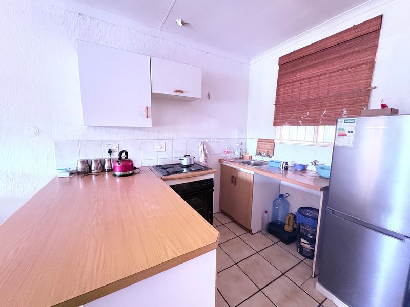 A compact kitchen featuring laminate countertops, built-in cabinetry, an electric hob with oven, and tiled flooring, offering a functional space with potential for modernization.