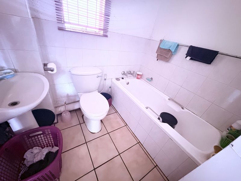 A functional bathroom featuring a pedestal basin, toilet, and bathtub with tiled walls and flooring, requiring cosmetic updates to improve its overall condition.
