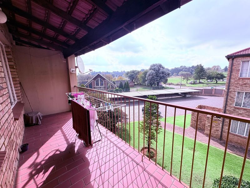 A covered balcony featuring tiled flooring and a metal balustrade, offering an elevated view of the complex grounds and surrounding neighborhood.