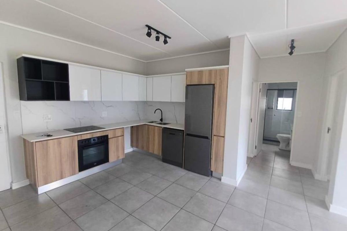 Modern open-plan kitchen featuring sleek two-tone cabinetry, stone countertops, integrated appliances, and neutral tiled flooring, leading to an adjacent bathroom.