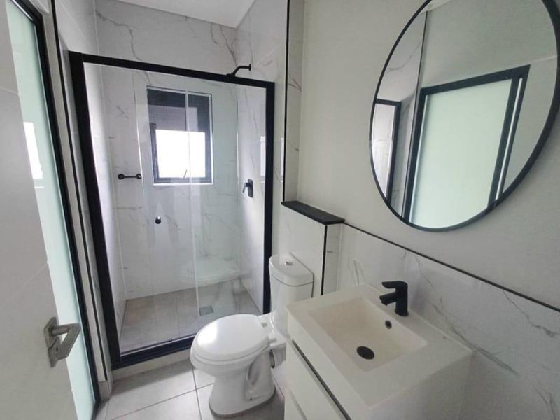 Modern bathroom featuring a walk-in shower with black-framed glass, a vanity basin with black tapware, and elegant marble-look wall tiles.