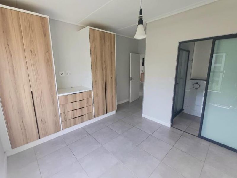 A clean, modern bedroom featuring neutral tiled flooring, ample built-in wooden cabinetry, and direct access to an en-suite bathroom.