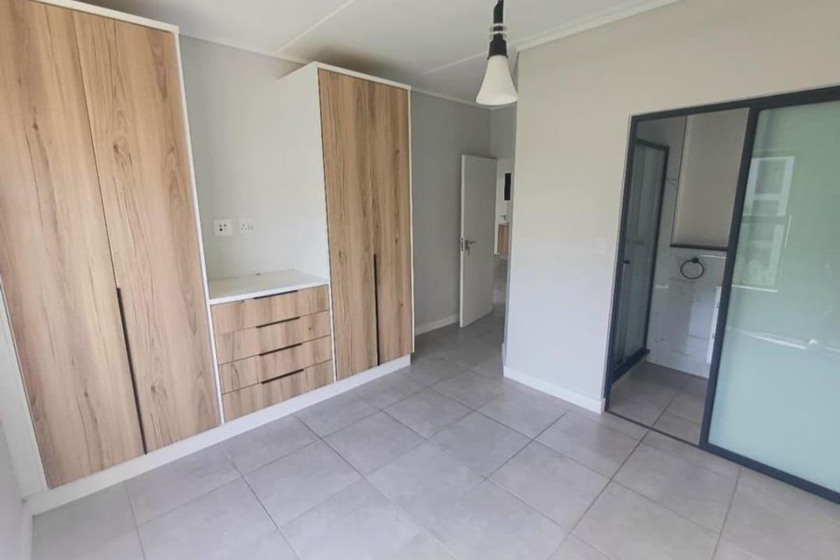A clean, modern bedroom featuring neutral tiled flooring, ample built-in wooden cabinetry, and direct access to an en-suite bathroom.