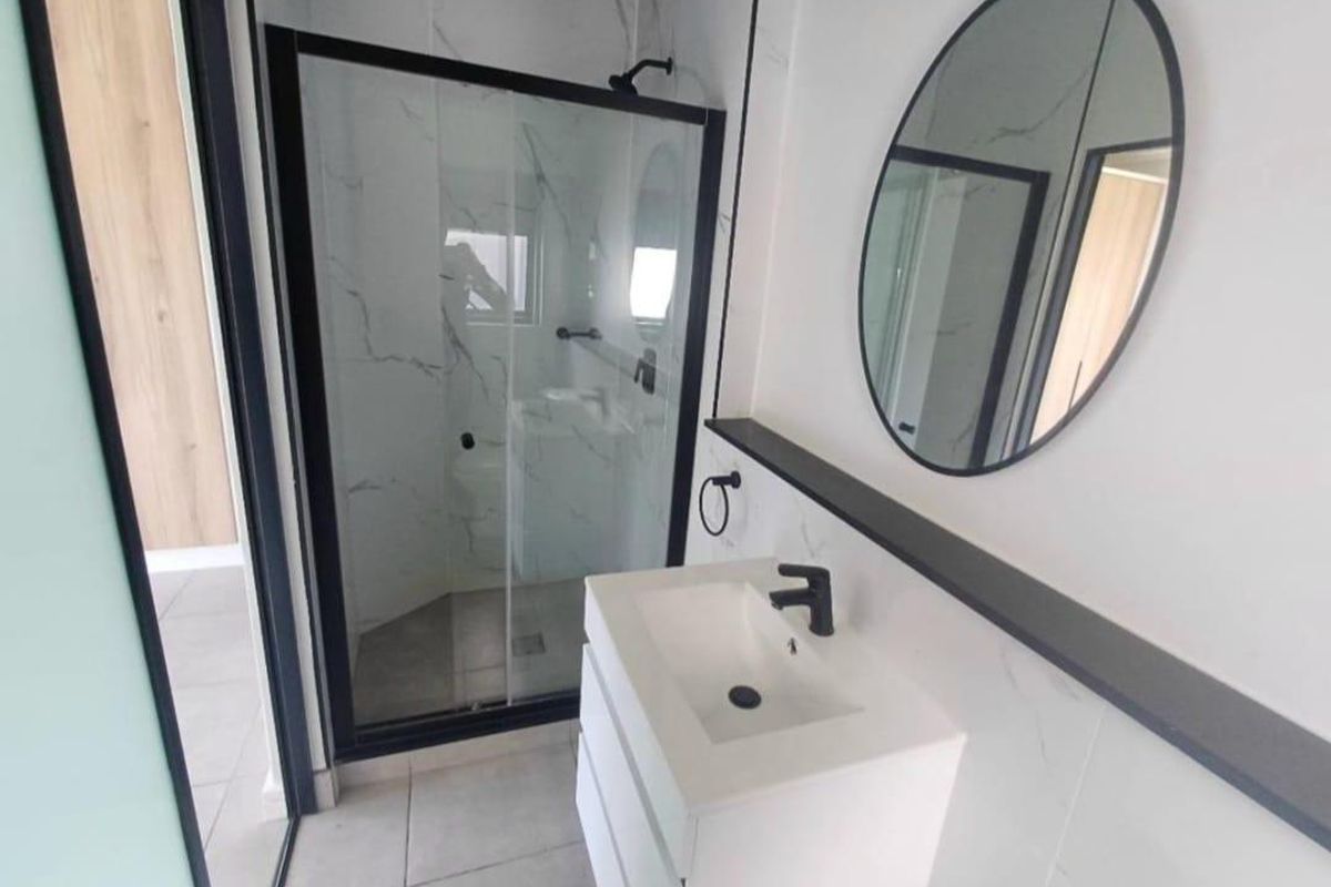 Modern bathroom featuring a sleek vanity with black tapware, marble-look wall tiling, and a glass-enclosed shower with a black frame.