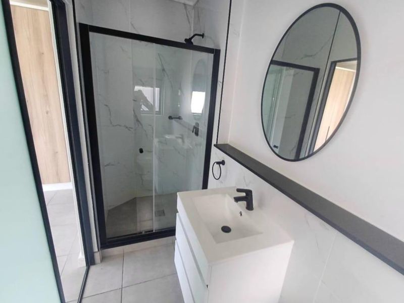Modern bathroom featuring a sleek vanity with black tapware, marble-look wall tiling, and a glass-enclosed shower with a black frame.