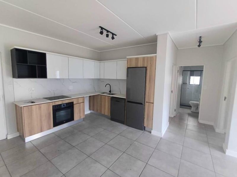 Modern open-plan kitchen featuring sleek two-tone cabinetry, stone countertops, integrated appliances, and neutral tiled flooring, leading to an adjacent bathroom.
