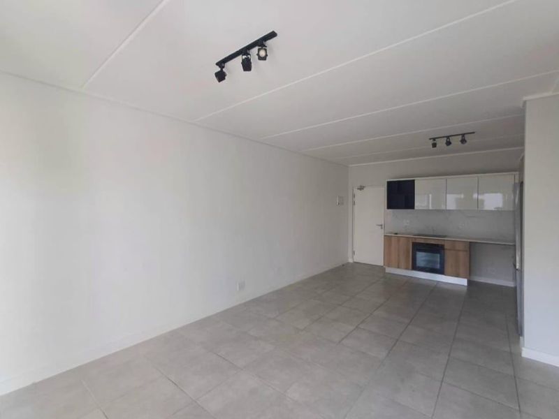 An open-plan living and kitchen area featuring modern track lighting, neutral tiled flooring, and contemporary kitchen cabinetry with a built-in oven.