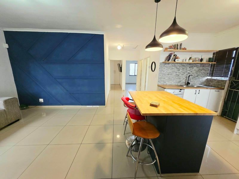 Modern open-plan living area featuring a kitchen island with wooden countertop, tiled flooring, and a striking blue feature wall.