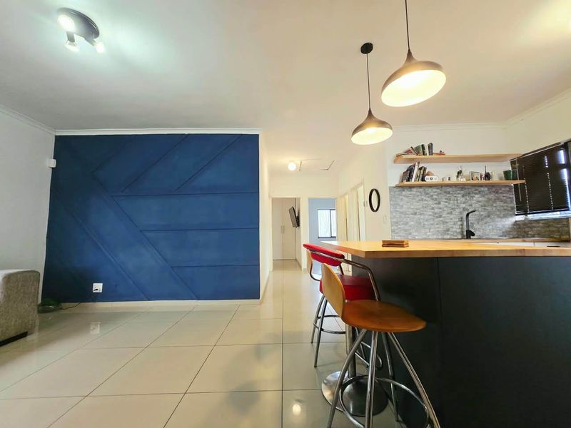 Modern open-plan living area featuring a kitchen island with breakfast bar, tiled flooring, and a striking blue geometric feature wall.