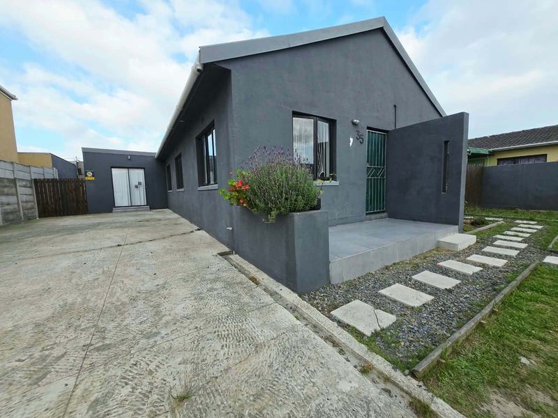 Front exterior view of a modern grey-painted house featuring a concrete driveway, tiled entrance porch, and a stone pathway leading to the front door.