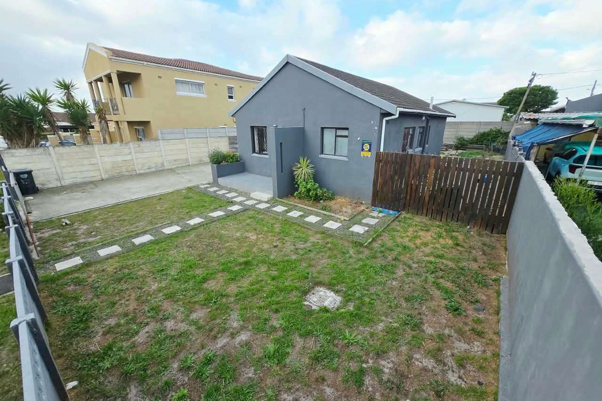 A rear view of the property featuring a private garden with a lawn, paved walkway, and perimeter boundary walls.