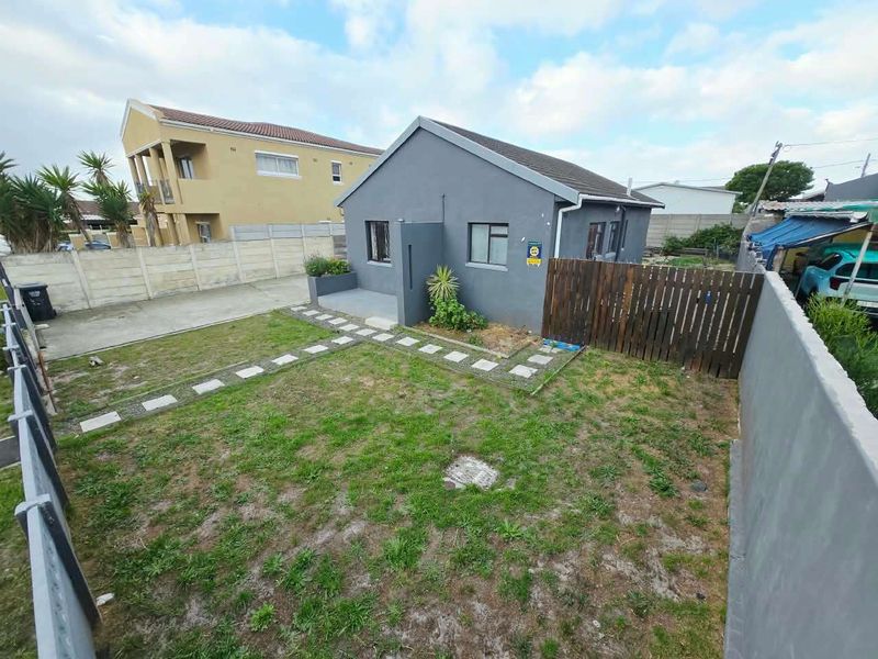 A rear view of the property featuring a private garden with a lawn, paved walkway, and perimeter boundary walls.