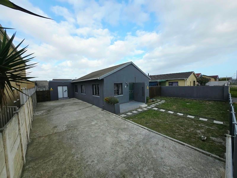 Front view of a detached house featuring a large concrete driveway, a private front garden with a paved path, and secure perimeter walling.