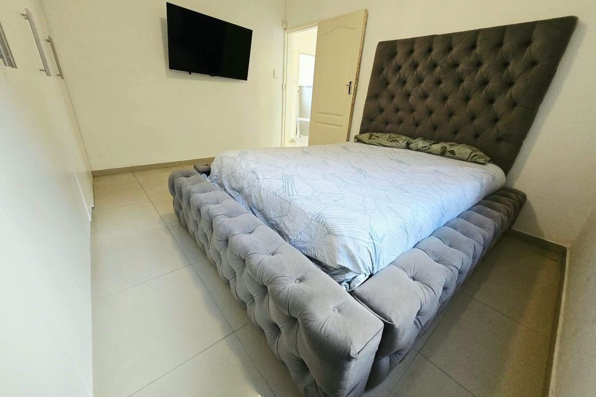 A well-maintained bedroom featuring neutral tiled flooring and built-in storage cupboards.