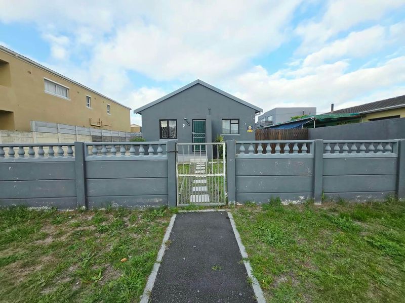Front view of a detached house featuring a grey painted facade, secure metal gate, and a paved walkway leading to the entrance.