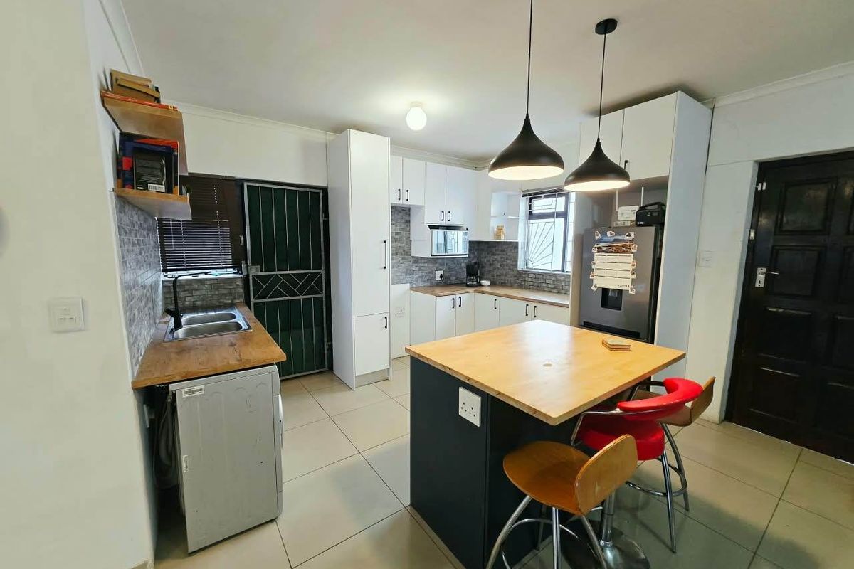 Modern kitchen featuring white cabinetry, a central island with wooden countertop, tiled flooring, and a functional layout with integrated sink and storage.