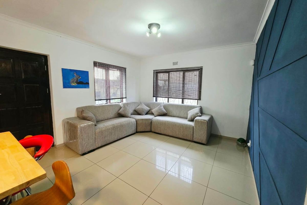 A bright living room featuring large format floor tiles, a dark blue feature wall, and venetian blinds on the windows.