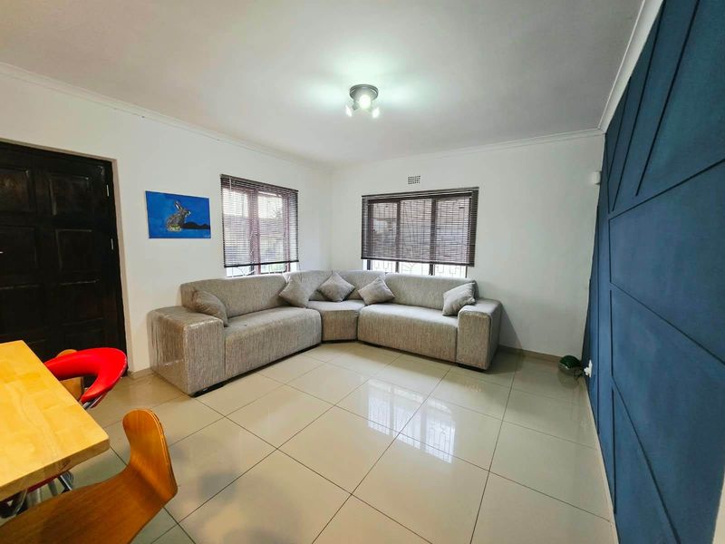 A bright living room featuring large format floor tiles, a dark blue feature wall, and venetian blinds on the windows.