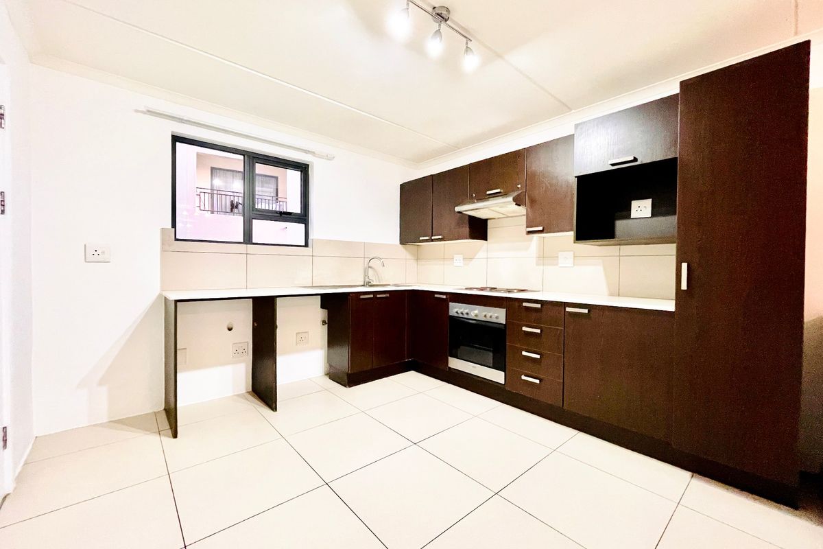 A clean, modern kitchen featuring dark wood cabinetry, built-in oven and hob, tiled flooring, and a functional layout with ample counter space.