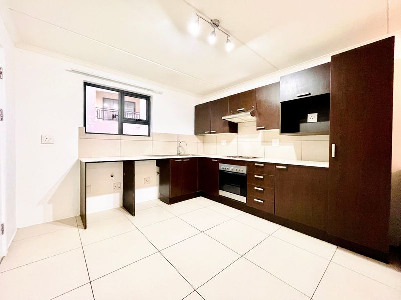 A clean, modern kitchen featuring dark wood cabinetry, built-in oven and hob, tiled flooring, and a functional layout with ample counter space.