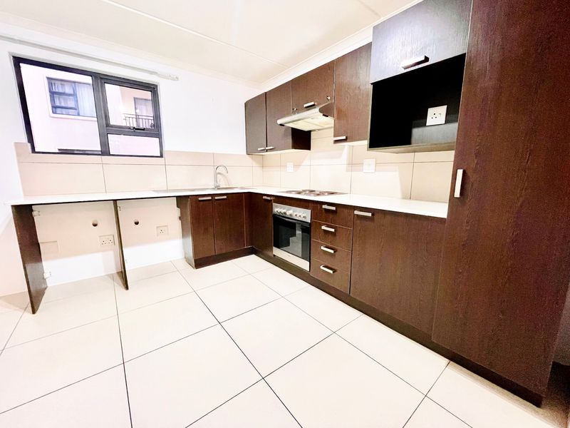 A clean, modern kitchen featuring dark wood cabinetry, built-in oven and hob, tiled flooring, and a neutral tiled backsplash.