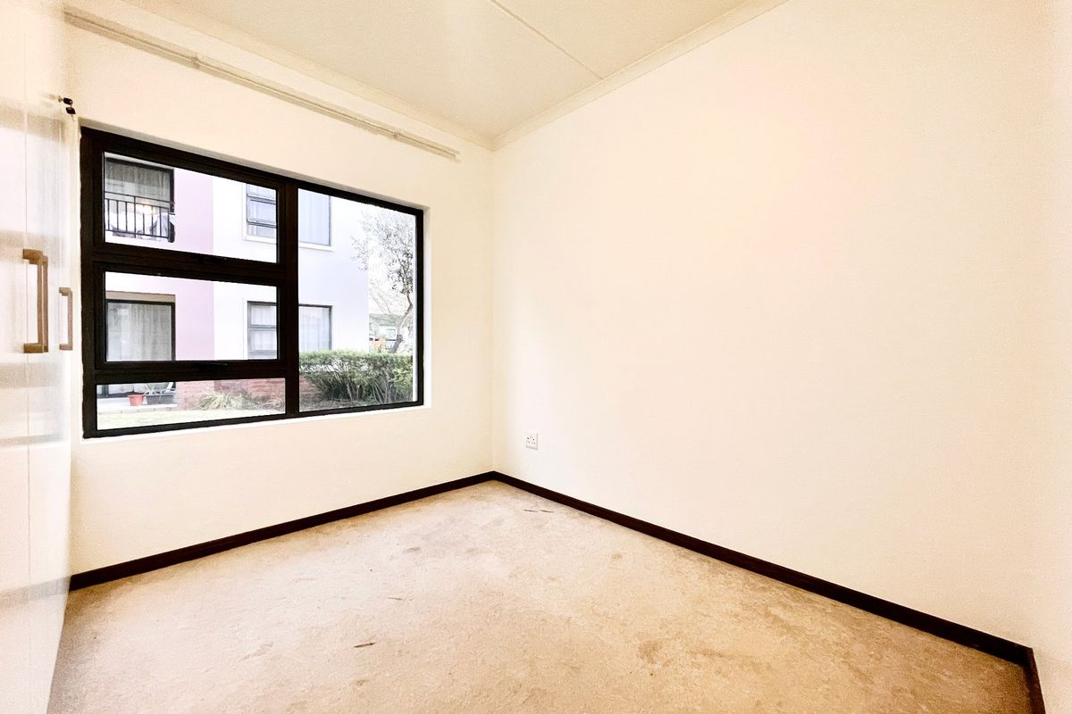 An empty bedroom featuring a built-in cupboard, aluminium window frame, and carpet flooring, offering a blank canvas for personalization.