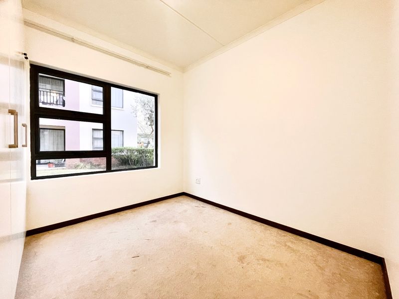 An empty bedroom featuring a built-in cupboard, aluminium window frame, and carpet flooring, offering a blank canvas for personalization.