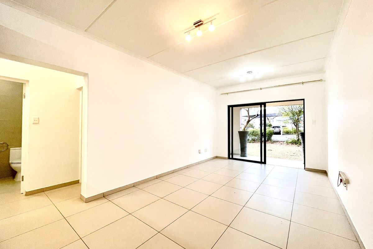 A bright, empty living area featuring neutral tiled flooring, modern ceiling lighting, and a sliding glass door providing access to the exterior.