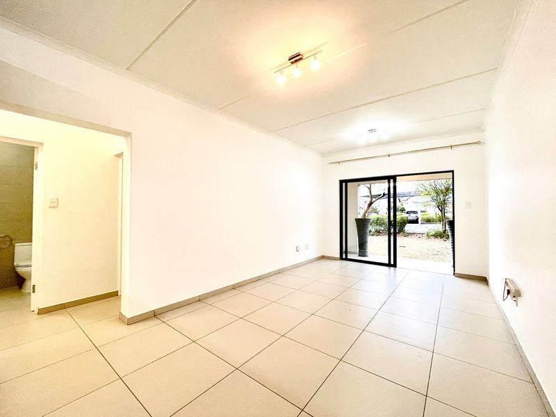 A bright, empty living area featuring neutral tiled flooring, modern ceiling lighting, and a sliding glass door providing access to the exterior.
