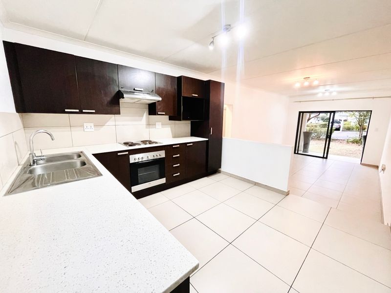 Open-plan kitchen and living area featuring dark wood cabinetry, modern appliances, tiled flooring, and direct access to an outdoor patio through sliding glass doors.