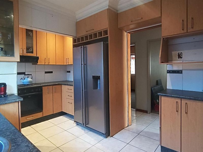 A functional kitchen featuring wood-tone cabinetry, dark laminate countertops, tiled flooring, and built-in appliances, offering a practical layout with potential for modern updates.