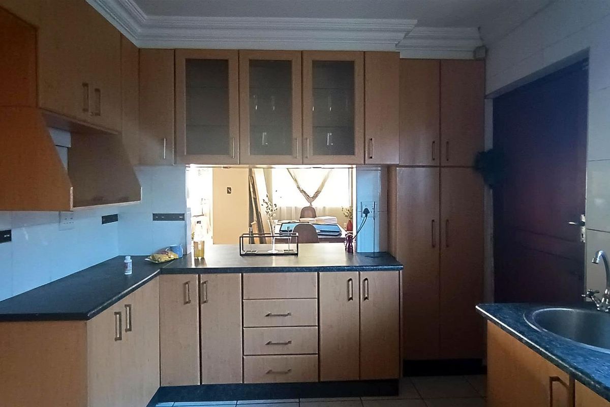 A functional kitchen featuring laminate cabinetry, dark countertops, and a stainless steel sink, with a pass-through window connecting to the adjacent living area.