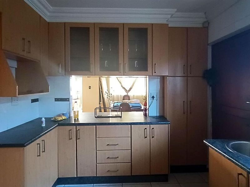A functional kitchen featuring laminate cabinetry, dark countertops, and a stainless steel sink, with a pass-through window connecting to the adjacent living area.